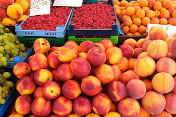 Beautifully laid out fruits at the farmers market. Peaches, bunches of white grapes, raspberries, blueberries on the counter of the bazaar for customers to choose. Fresh and natural fruits. Vegetarian