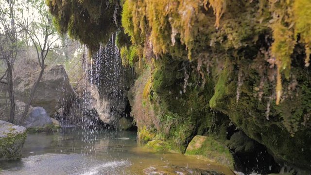 Gruta con cascada de agua con rocas verdosas de musgo en c&aacute;mara lenta