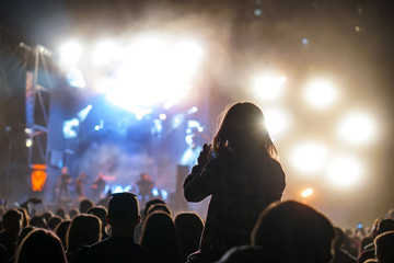 Child has fun on her parents' shoulders keeping hands with them at an outdoor rock music concert