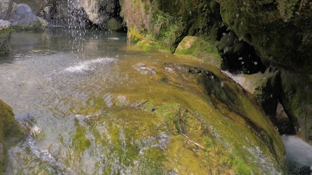 Gruta con caida en cascada de agua con rocas verdosas de musgo en c&aacute;mara lenta
