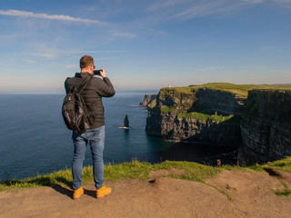 Male tourist taking picture of Cliff of Moher on his smart phone, Sunny warm day., Concept...