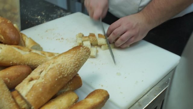 Cook cuts baguette bead into croutons on a white teflon cutting board