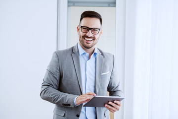 Attractive smiling white collar worker standing in living room, looking at camera and holding...