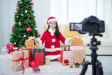 Obraz na płótnie Canvas Young beautiful asian girl in santa claus dress recording video blog about christmas gift at home