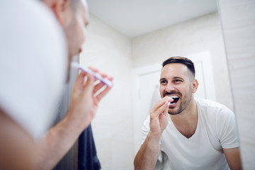 Reflection of good looking man brushing his teeth in morning. Daily routine.