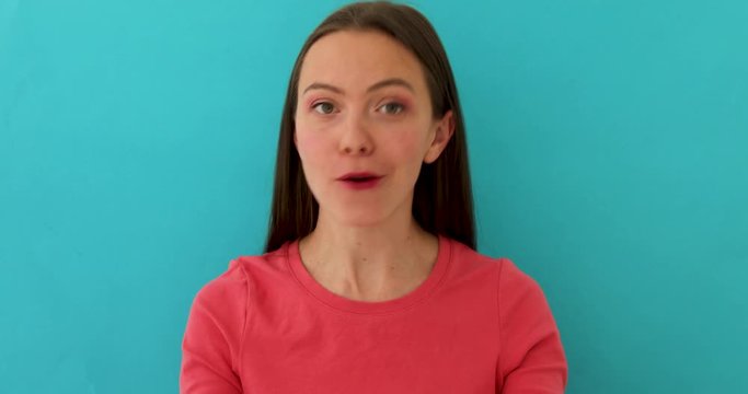 Sceptical woman in bright clothes rising eyebrow and gesturing while talking and standing over blue background
