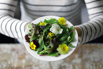 A plate of salad in the hands of a slender girl. Beautiful girl eating flowers salad. Diet concept. Healthy food concept.