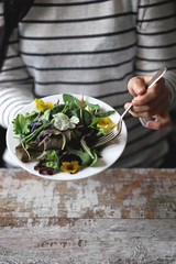 A plate of salad in the hands of a slender girl. Beautiful girl eating flowers salad. Diet concept. Healthy food concept.