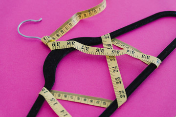 clothes hanger with measuring tape on pink background