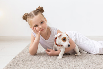people, children and pets concept - little child girl lying on the floor with cute puppy Jack Russell Terrier