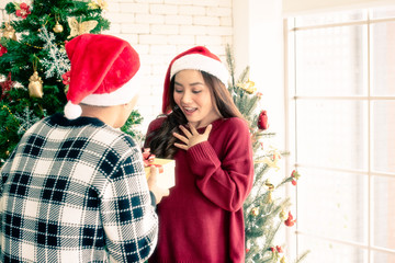 A couple with Santa's hat in the room, a beautiful woman is happy and surprised when she got a yellow gift box from her boyfriend on Christmas day. Copy Space