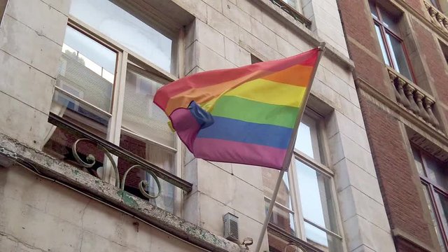Gay pride LGBT rainbow flag waves on an urban city apartment building