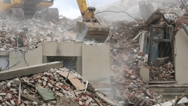 Close-up of bucket Excavator working to get rid of the rubbish in a demolition site. Demolition of the old industrial building.