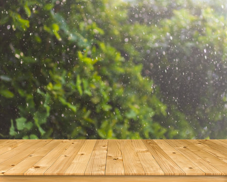 Empty old brown plank wooden board as mock up display shelf with blurred natural picture from fresh green leaves tree with group of fall droplet&rsquo;s motion and bokeh from hard rainy background.