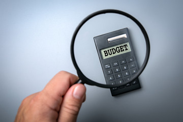 Budget concept. Calculator on white table. Man's hand, holding magnifying glass