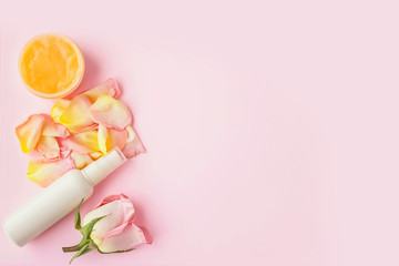 Open jar of cosmetic cream, white cosmetics bottle, rose and rose petals on pink background. Concept of natural spa cosmetics. Flat lay, top view, copy space.