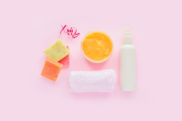 Open jar of cosmetic cream, white cosmetics bottle, soap and towel  on pink background. Concept of natural spa cosmetics. Flat lay, top view, copy space .