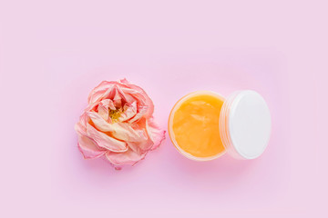 Open jar of cosmetic cream and rose on pink background. Concept of organic spa cosmetics. Flat lay, top view, copy space.