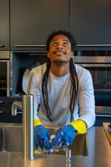 Young African-American man with dreadlocks washing in the kitchen.