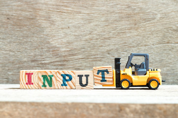 Toy forklift hold letter block t to complete word input on wood background