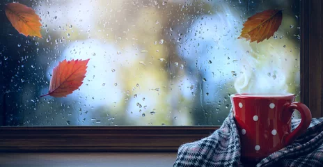 Deurstickers red cup with hot drink and wet autumnal window  Autumn season background © Konstiantyn