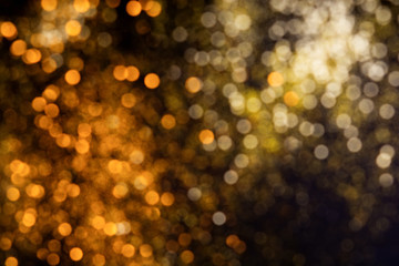 Abstract blurred glitter bokeh background in gold and orange, on black