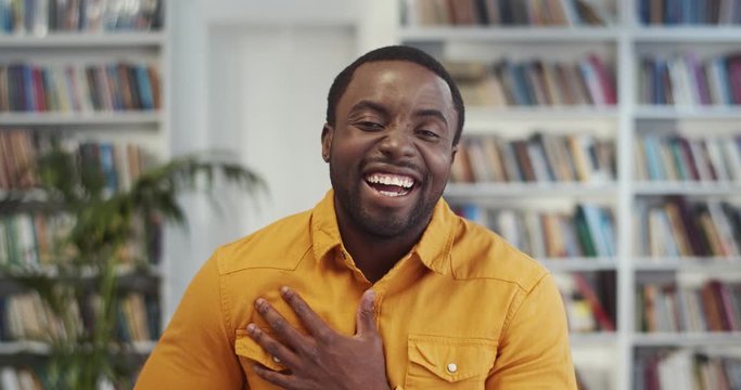 Portrait shot of the African American handsome young stylish man in yellow shirt laughing cheerfully to the camera in the library.