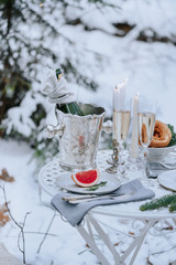 Decorated table for a romantic dinner with candles, sparkling wine and fruit in the winter forest