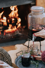 Women's hands pour mulled wine outdoors on the background of a burning fireplace