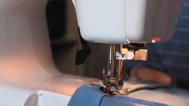 A man tailor in a sewing machine makes seams. Close-up of sewing: the beginning of the movement of needle, stitching, reverse, thread trimming after the end of needlework