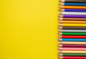 Crayons on yellow background with copy space. Back to school. Colored pencils next to each other top view. Marketing and development theme. 