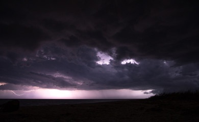 Fototapeta na wymiar Massive thunderstorm with black cloud over the sea and lightings on the horizon
