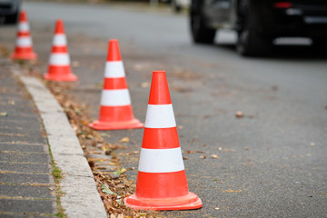 A row of traffic cones standing on a street along the curbstone of the pavement to prevent other...
