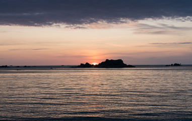 Obraz na płótnie Canvas sunset at the beach with a calm ocean and rocks and reefs under an orange and blue sky