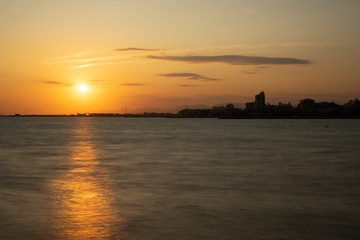 Atardecer en Santa Pola, Alicante, España. Primer plano de mar con reflejos de sol y horizonte de cielo naranja con nubes