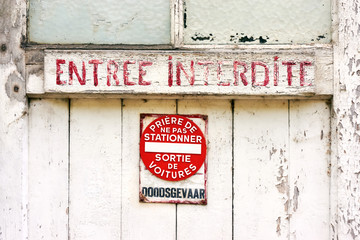 Entree Interdite. Old weathered white door in Belgium with red painted text forbidden entry in french and no parking sign     