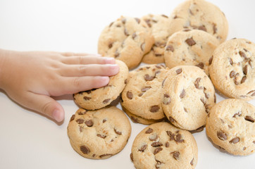 Child's hand on cookies with dark chocolate chips on the white background. Dessert or pastries