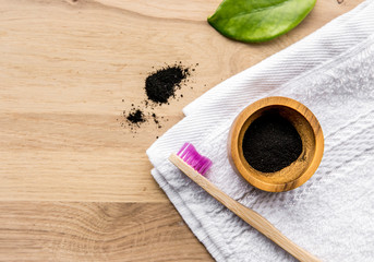 Raw activated charcoal powder in wooden cup and natural bamboo toothbrush next to it, green leaf and bath towel. Charcoal toothpaste concept. Lot of copy space.