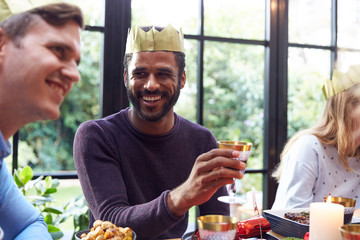 Group Of Friends Sitting Around Table At Home For Christmas Dinner Drinking Wine