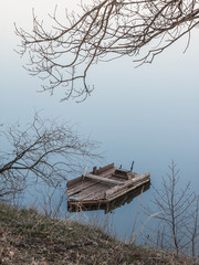 Abandoned old homemade wooden boat at water surface of pond at sunrise