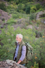 Tourist man with a gray beard with a backpack on his shoulders against the backdrop of the gorge, rocks and stones,