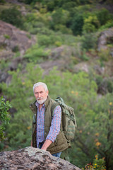 Tourist man with a gray beard with a backpack on his shoulders against the backdrop of the gorge,...
