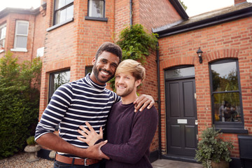 Portrait Of Excited Gay Male Couple Standing Outside New Home On Moving Day Together