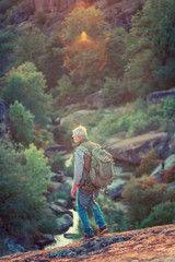 Old tourist with gray hair and beard backpack is hiking in canyon