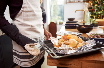 Close Up Of Man Taking Roast Chicken Out Of Oven For Christmas Dinner