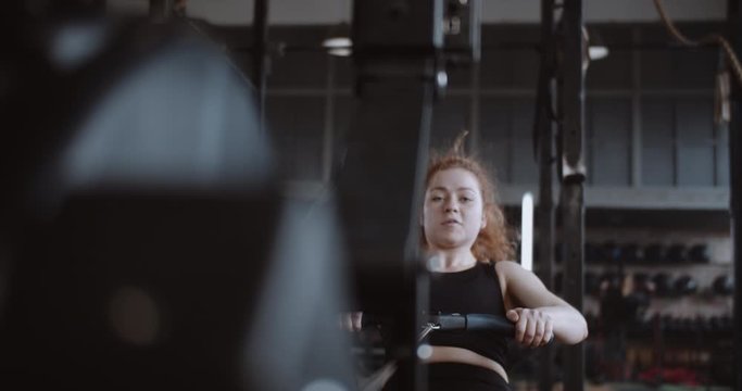 Active lifestyle and sports, young beautiful happy red haired woman exercising on rowing machine in gym slow motion.