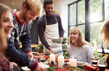 Group Of Friends Sitting Around Dining Table At Home As Christmas Dinner Is Served