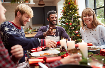 Group Of Friends Sitting Around Table Making A Toast At Home And Eating Christmas Dinner