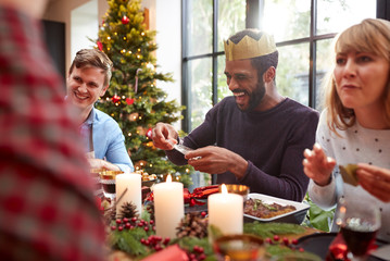 Group Of Friends Sitting Around Table At Home For Christmas Dinner Reading Jokes From Crackers