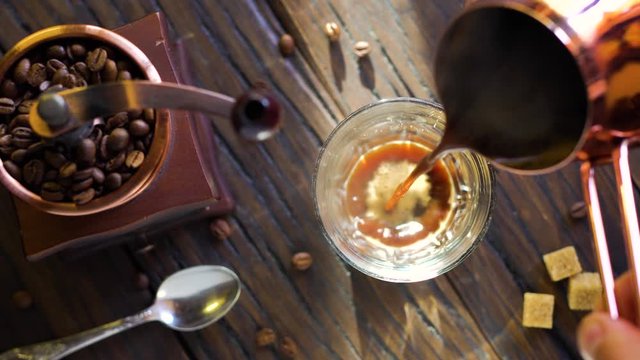 Freshly brewed coffee from cezve is poured into a coffee cup. Steam comes out of the cup, an old coffee grinder is in the composition. 4K video.